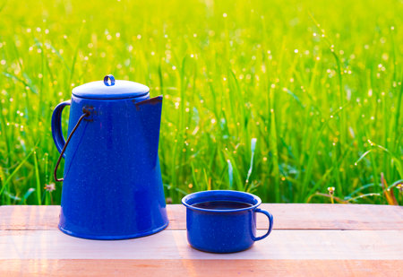 Kettle, blue enamel, and coffee mugs On an old wooden floor, Blurred background of rice fields at sunrise.の写真素材