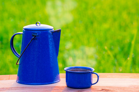 Kettle, blue enamel, and coffee mugs On an old wooden floor, Blurred background of rice fields at sunrise.の写真素材