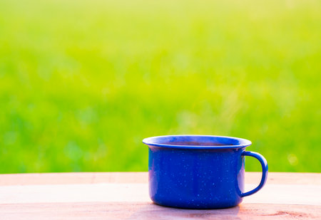 Kettle, blue enamel, and coffee mugs On an old wooden floor, Blurred background of rice fields at sunrise.の写真素材
