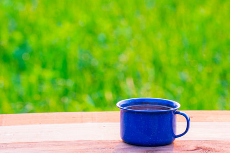 Kettle, blue enamel, and coffee mugs On an old wooden floor, Blurred background of rice fields at sunrise.の写真素材