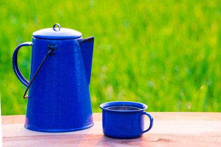 Kettle, blue enamel, and coffee mugs On an old wooden floor, Blurred background of rice fields at sunrise.の写真素材