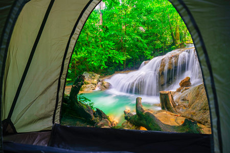camping tent, looking from inside the tent to view the emerald blue water in Erawan National Park. Erawan Waterfall is a beautiful natural rock waterfall in Kanchanaburi, Thailandの写真素材