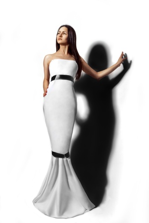 Pretty girl in long white dress and shadow on backgroundの写真素材