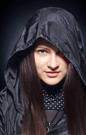 portrait of a beautiful young girl in the hood on dark backgroundの写真素材