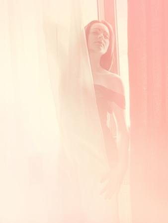 petite young girl stand near window in pink lightの写真素材