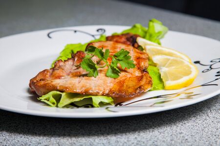 meat decorated with fresh herbs and lemon on a white plateの写真素材