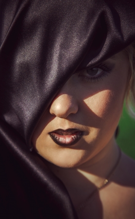 beautiful young girl looking at camera with one eye outdoors in the hoodの写真素材