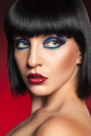 Sexy brunette with professional make up looking away in studio on red backgroundの写真素材