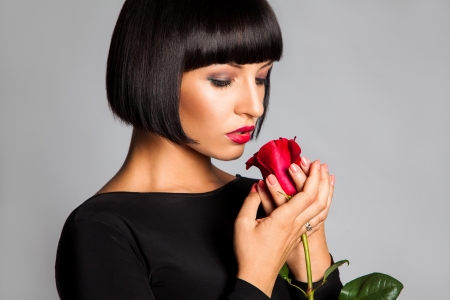 Beauty adult girl with red rose looking down in studio on gray backgroundの写真素材