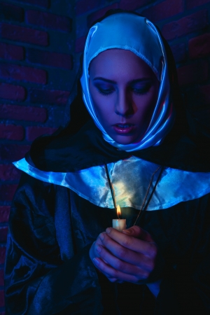 cold tones portrait of female monk with candle in hands near brick wallの写真素材