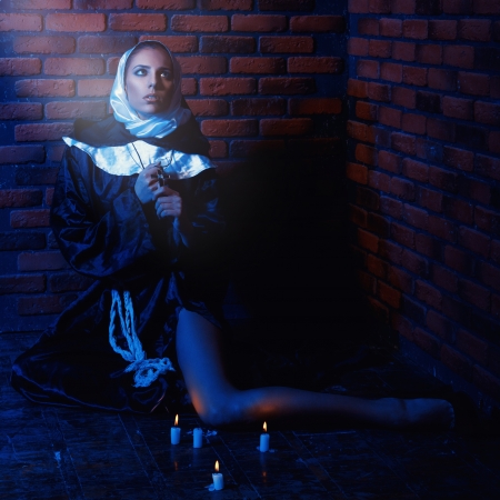 square photo of nun sitting near brick walls with candles on floorの写真素材