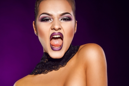 Pretty young woman screaming in studio on purple background in studioの写真素材