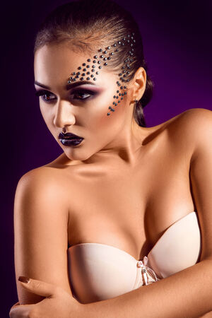 Vertical portrait of sensual adult girl with diamonds on face in studio on purple backgroundの写真素材