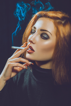 smoking red hair woman in studio on black の写真素材