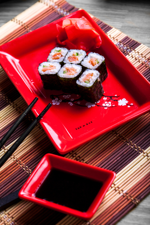 Japanese roll with salmon on red plate in restaurantの写真素材