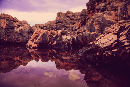 photo of rocks and their reflection in the sea at sunriseの写真素材