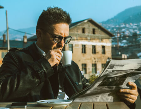 Beautiful adult business man drink coffe and read newspaper outdoorsの写真素材