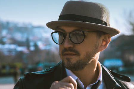 Glamour portrait of beauty man in hat and glasses looking away outdoors at daytimeの写真素材