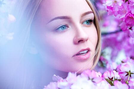 Adorable young blonde in blooming pink flowers. Spring timeの写真素材