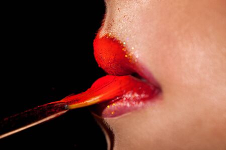 macro photo of Girl applies lipstick with brush in studio on black backgroundの写真素材