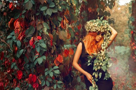 portrait of redhead young girl with wreath of hop on head outdoors in the forest