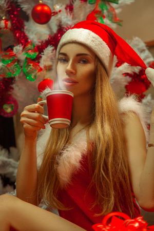 Pretty blonde in santa hat drinking a hot drink.の写真素材