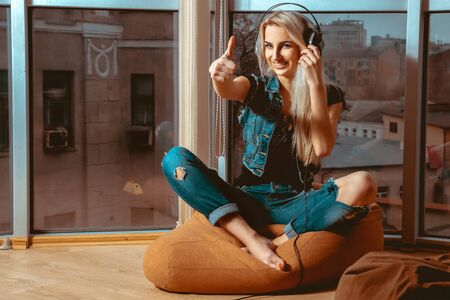 cool young blond woman listening to good music in headphones and shows class. Girl listening to the music. Blonde listen to the music in headphones. Music in headphones.の写真素材