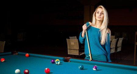 Fashion portrait of beautiful young blonde girl plays billiard.