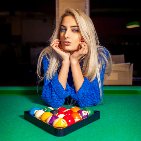 Portrait of young beautiful blonde girl with pyramid of pool balls.