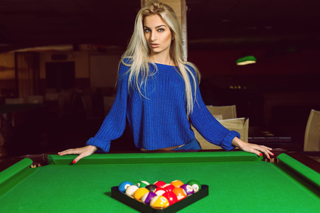 Lovely adult blonde posing near a billiard table with a pyramid of balls.の写真素材