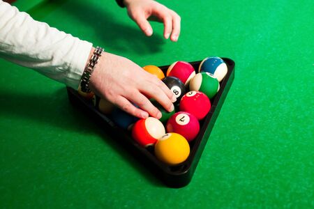 male hands to place the balls in the triangle to play eight ball at pool table.