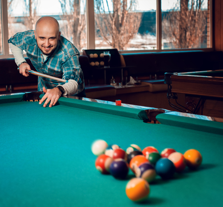 man begins to play a game of billiards and breaks pyramid of balls on the table.