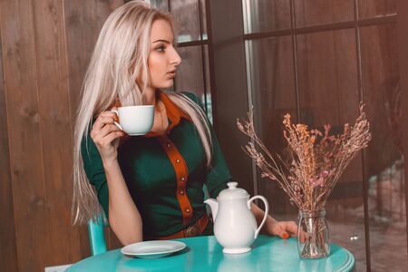 Lovely young blonde girl drink coffee and looking away at the window. Beautiful girl in cafe with ciup of tea looking away.の写真素材