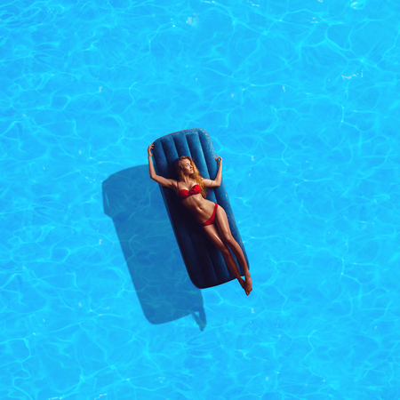 beauty tan glamour lady in red bikini sunbathing by the blue pool outdoors