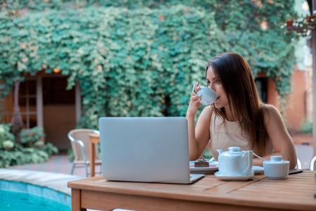 horizontal portrait of beautiful young woman with cup of tea and laptop outdoorsの写真素材