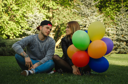 couple sits on the grass with a lot of colorful balloons in female hands and having fumの写真素材
