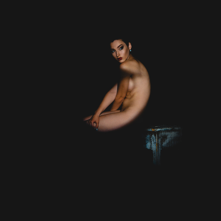 square portrait of nude young brunette lady with shadows on her body sits on a chair and looking away in studio on black backgroundの写真素材