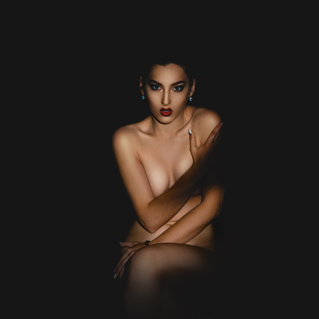 Serious young brunette woman with red lips looking at the camera in studio on black backgroundの写真素材