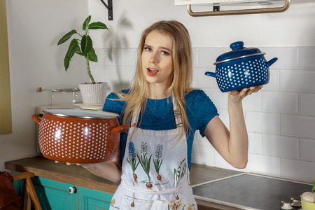 Funny blonde woman with two pans in her hands in the kitchenの写真素材