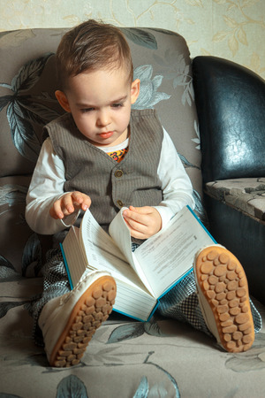 vertical portrait of young boy in elegance suit read a book and sits on a sofaの写真素材