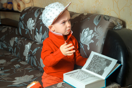 elegance young boy in red suit and cap with stars read a book and a sofaの写真素材