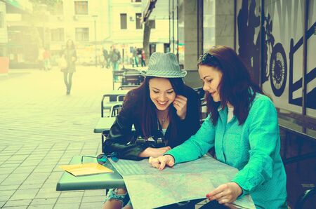 two women sitting at a table on the street and study the map of the city and having funのeditorial素材