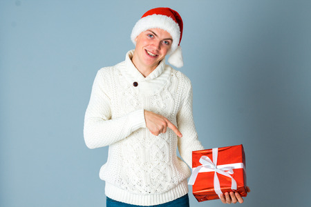 young cheerful man with gift box in hands and santa hat looking at the camera and smiling in studio