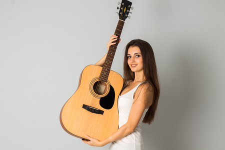 portrait of cheerful young girl with guitar in hands posing in studio smiling on cameraの写真素材