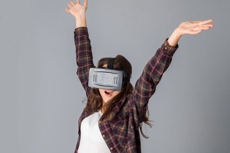 portrait of young pretty girl in virtual reality helmet in studio on grey background