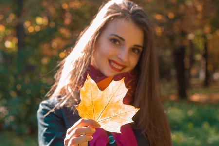 beautiful young girl smiling and holding a maple leaf in his hand closeupの写真素材