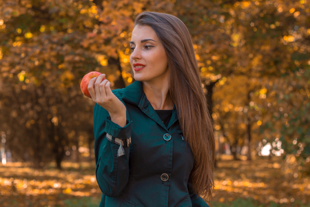 beautiful girl with long hair stands in the park looks away and keeps Apple in handの写真素材