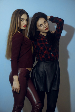 portrait of two young pretty stylish women looking at the camera in studio on blue backgroundの写真素材