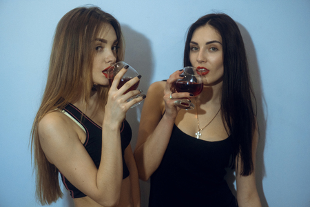sexy young girls drinks wine and posing in studio on blue backgroundの写真素材