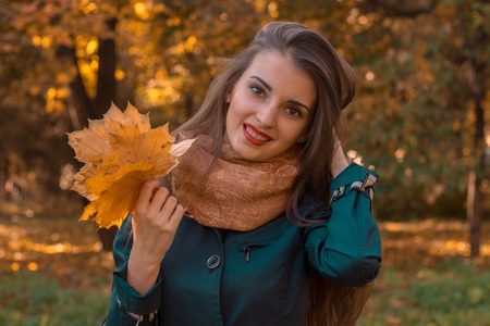 beautiful young girl stands and smiling in the Park keeps the hair with one hand while the other hand holds the leaves closeupの写真素材